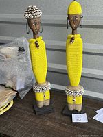 Two yellow beaded Namji Dolls from Cameroon standing side by side with their unique adornments.