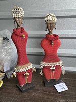 Front and side view of two Namji beaded fertility dolls with red beads, cowrie shells, and wooden bases.
