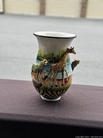 Front view of the ceramic vase featuring 3D giraffe and cheetah animal figures with a detailed painted nature scene.