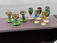 Photo showing 6 hand painted art glass wine glasses and 3 vintage cordial glasses with green ribbed stems on display