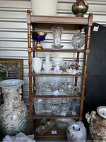 Full view of the wood shelving unit with glass and wood shelves, showing the frame and the shelves with various glassware items on them for scale.