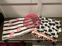 Two folded tablecloths and a pink mesh food cover on a surface.