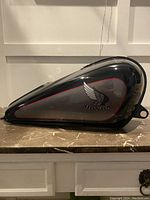 Side profile of Honda gas tank showing black and gray paint with red outline and Honda wing logo