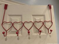 Pink metal over-the-door hanger with five heart-shaped hooks hung on a white door showing some wear.