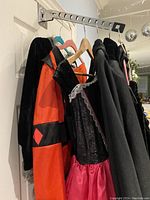 Image showing hanging Halloween costumes on hangers including a red and black jester outfit and a black and red dress with lace detail.