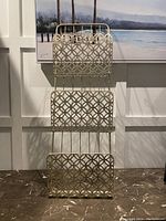 Front view of the new 3-tier metal rack with gold finish, showing decorative geometric circular cutout pattern on each tier and overall vertical structure.