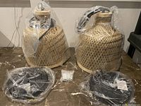 Two bamboo hanging light shades with wiring and mounting components wrapped in plastic on marble surface.