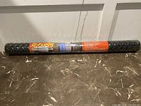 Overall view of the rolled BBQ grilling mat on a marble surface, showing the product labeling and packaging.