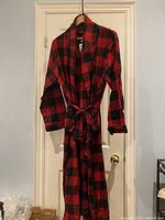 Red and black plaid men's robe hanging on door, showing full length and belt tied at waist