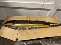 Partially opened cardboard box showing gold-colored metal tubes wrapped in plastic inside.