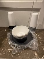 4 tall black and white striped tumblers, 6 white round bowls stacked inside a large black bowl, on marble countertop
