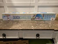 Photo of the new Quick Shelter tent in original box packaging, displayed on a table.