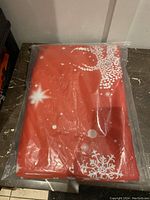 Folded red curtain panel with white reindeer and snowflake designs in plastic packaging