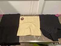Three slimming under garments laid out on a surface: two black and one beige, all new with tags visible on the black and beige garments.