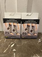 Two boxed packages of plantar fasciitis compression sleeves, showing the front of both boxes with branding and product image.