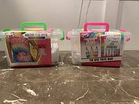 Photo shows two clear plastic kits with handles containing tie dye supplies. One kit labeled Neon Tie Dye Fashion Design Kit includes a tank top and dye colors. The other is a Tie Dye Tote Bag kit with dyes and tote bag.