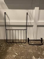 Two black metal over-the-door holders placed side by side on a marble surface in front of a white paneled wall.