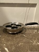 Side view of a stainless steel pan with black handle and four non-stick egg cups inside, marked 'Potobelo' on the side.