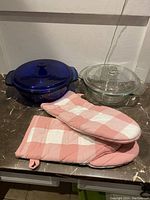 Two Pyrex bowls in clear and dark blue glass with matching lids and pink and white checkered oven mitts.