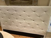 Front view of white upholstered queen size headboard with diamond tufting and jeweled accents.
