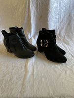 Two pairs of women's black booties displayed side by side on white textured fabric background