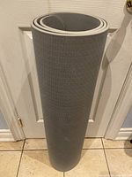 Gray yoga mat rolled up standing vertically against a white door, showing entire length and visible surface texture.