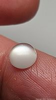 Close-up view of the white moonstone cabochon gemstone on finger showing translucency and flash.