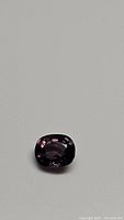 Close-up photo of a purple cushion cut spinel gemstone showing its shape, color, and internal reflections.