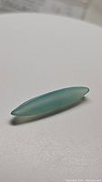 Marquise shaped natural chalcedony gemstone in arctic blue teal color on white background, showing translucent quality and smooth surface.
