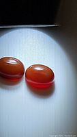 Two oval cabochon carnelian gemstones on white surface under spotlight showing translucent deep red-orange color.