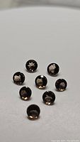 Eight round diamond-cut natural smokey quartz gemstones, showing reflections and clarity, arranged on white surface.