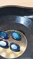 Four oval cut Ethiopian black opals with visible multicolored flashes in a tray.