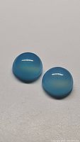 Close-up photo of the pair of round cabochon icey blue chalcedony gemstones showing their color and surface polish.