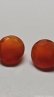 Two round mandarin orange carnelian gemstones with faceted cuts.