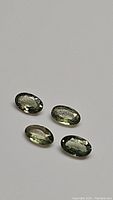 Four oval-cut mint green sapphires laid on a flat grey surface showing facets and clarity.