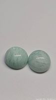 Close-up of matched pair of baby blue amazonite polished cabochon gemstones showing natural veining and smooth dome shape.