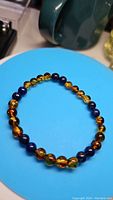 Photo showing the bracelet with alternating blue lapis lazuli beads and translucent amber beads against a blue background.