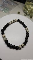 Photo showing round black lavastone beads and distinctive white Dalmatian jasper beads with black spots on a stretchy bracelet, placed on a white surface.