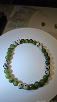 Natural green jade and Dalmatian jasper gemstone stretchy bracelet laid flat on white surface showing bead colors and pattern details.