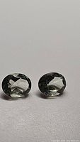 Pair of natural green Amethyst (Prasiolite) gemstones, oval cut, shown resting on flat surface.