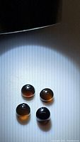 Four rounded transparent chocolate onyx gemstones with smooth polished surfaces. Stones show translucence in lighting, distinctly brownish compared to typical opaque black onyx.