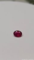 Close-up photo of natural oval cut ruby 1.03ct on plain white background showing facets and deep red color.