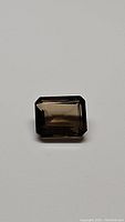Top view photo of 3.42 carat emerald cut natural smokey quartz gemstone on plain background showing color and clarity.