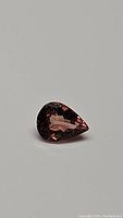 Close-up image of 1.09 carat pear cut padparadscha tourmaline showing pinkish-orange color and internal features.