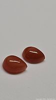 Close-up image of two pear-shaped peach moonstone cabochon gemstones on a plain background, showing smooth polished surfaces and deep peach color.