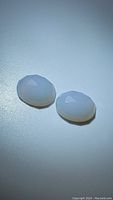 Two matching white chalcedony fancy cut gemstones shown from top angle on white surface, highlighting their facet cuts and pearly white color.