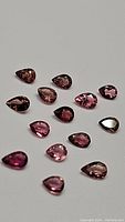 Photo of 14 pear cut natural pink tourmaline gemstones arranged on a flat surface showing varying shades of pink and good clarity.