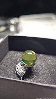 Close-up of the ring in a jewelry box showing the amber cabochon and leaf motif with emerald accent.
