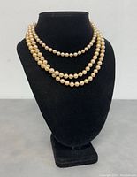 Front view of two vintage pearl necklaces displayed on black velvet bust, showing their length and pearl uniformity.