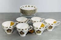 Set of six white bone china teacups each with matching saucers, all showing zodiac symbols and gold detailing, arranged with saucers stacked behind cups.